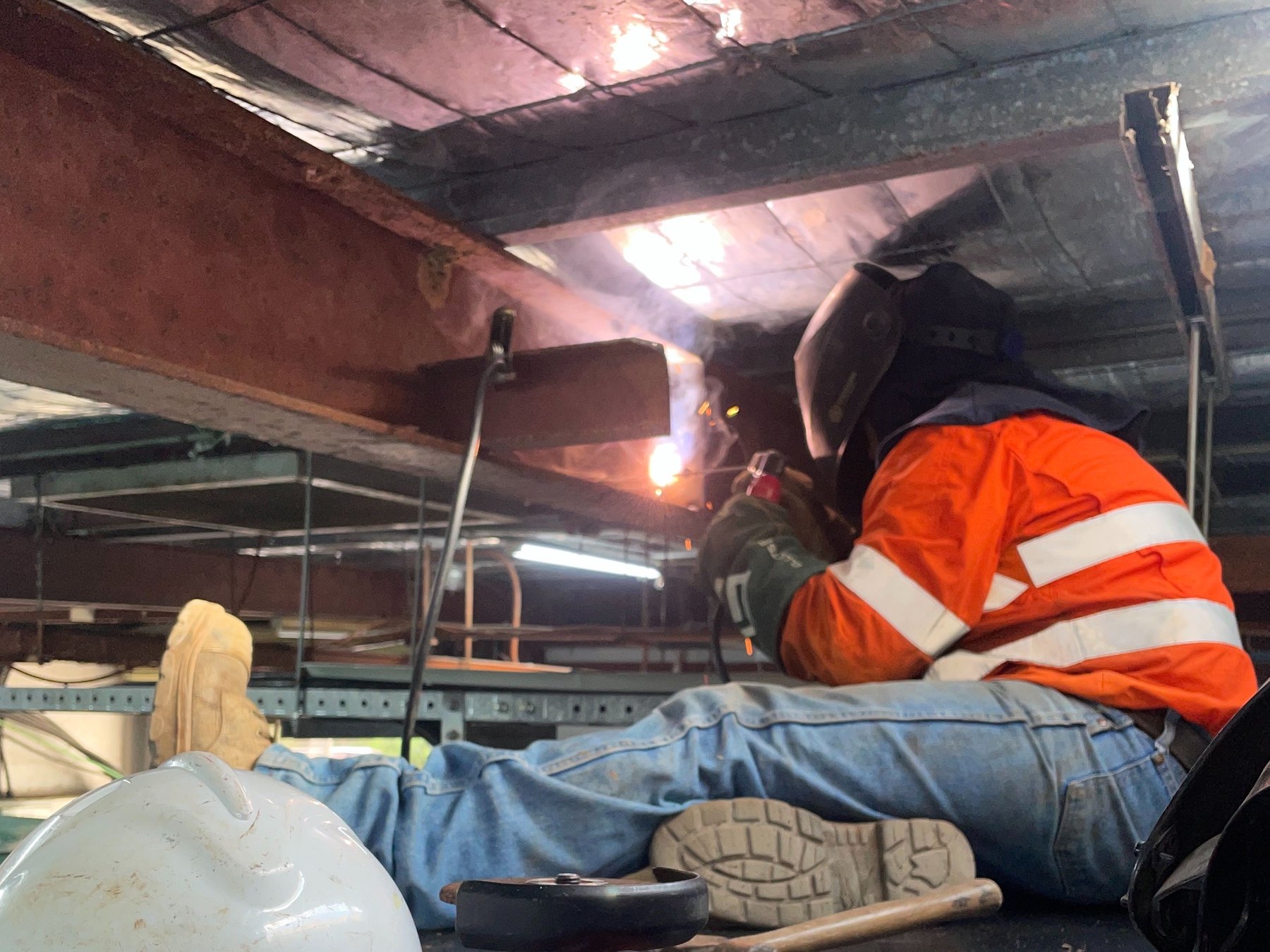 Vision welder performing structural steel modifications with Vision-branded hard hat in foreground